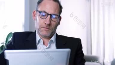 商人在他的办公室或酒店房间里用平板电脑iPad工作，而屏幕反射在他的眼镜上跟踪